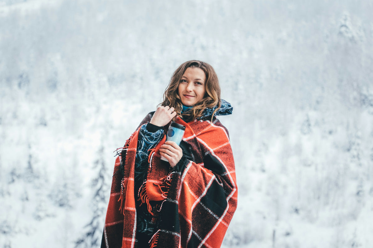 Woman wrapped in a red and black plaid wrap outdoors in a snowy forest